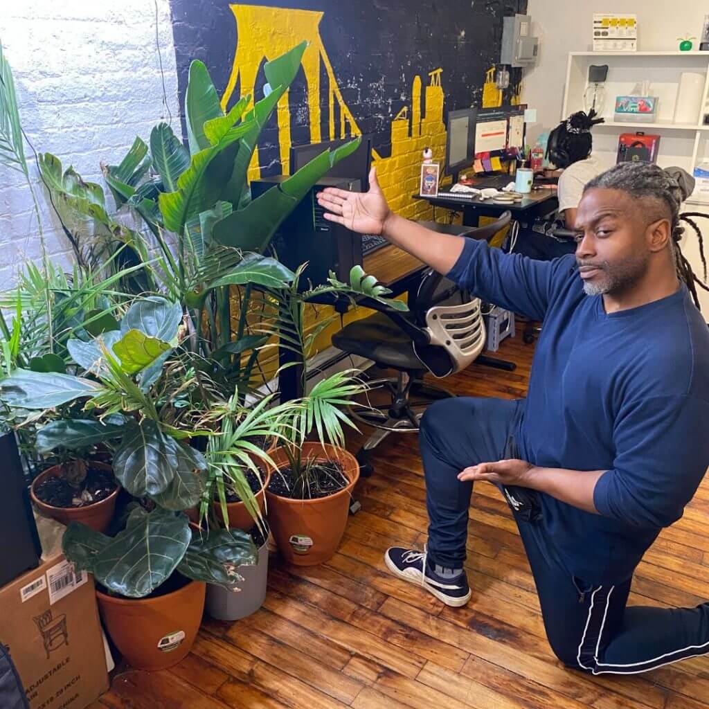 Coworker posing with all of his indoor office plants with grow lights above.